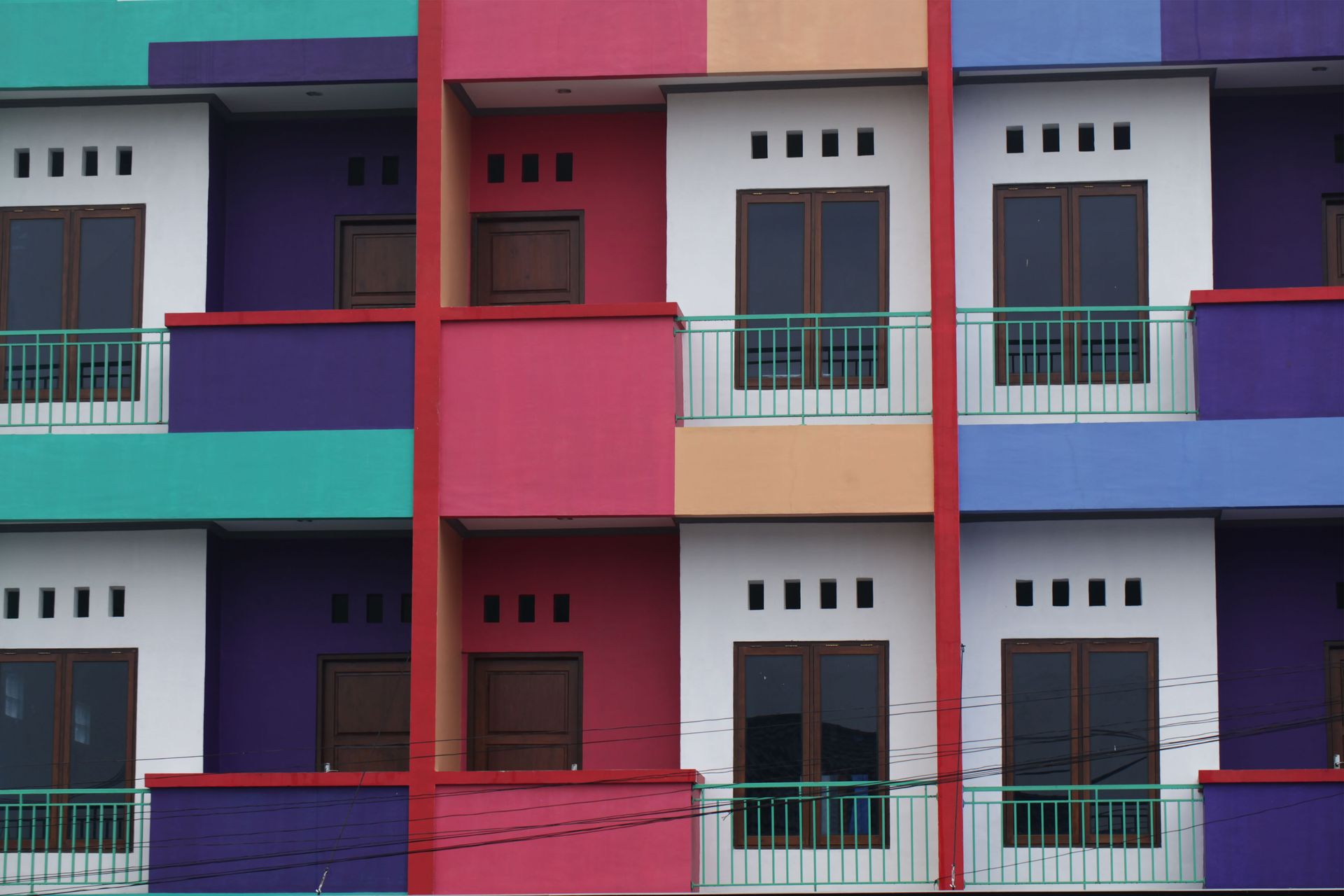 Vibrantly colored urban apartment building with balconies and windows in geometric pattern.